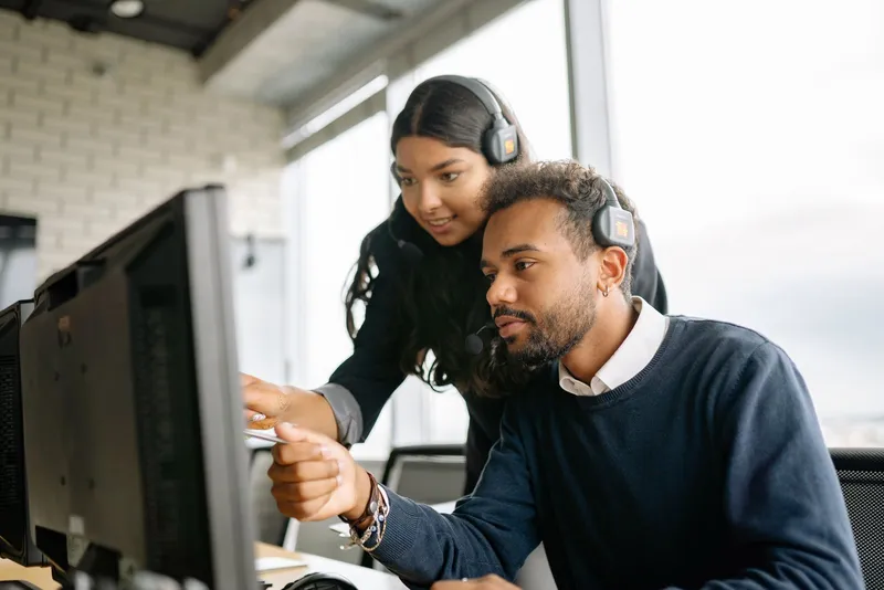 Two contact-centre agents with headsets working together at one screen