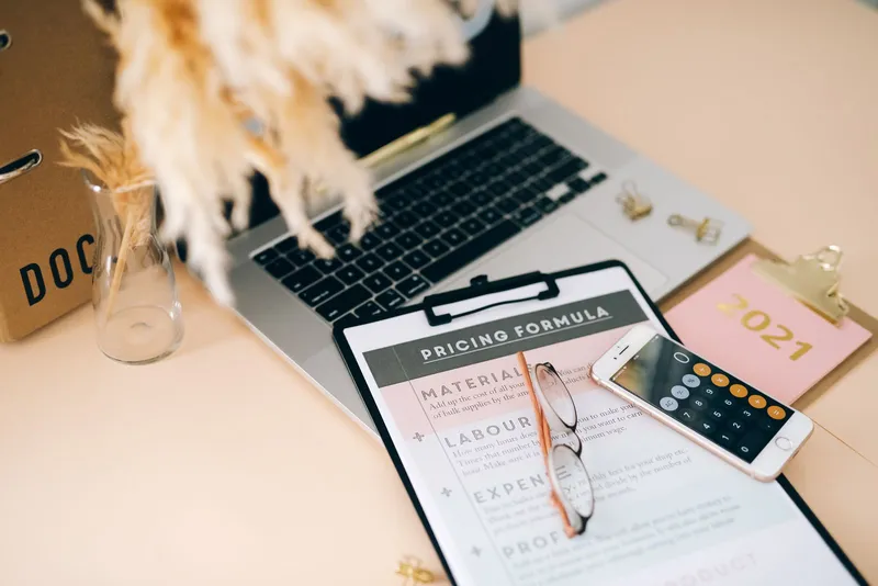 An office desk with a pricing document, a laptop and a calculator on a phone
