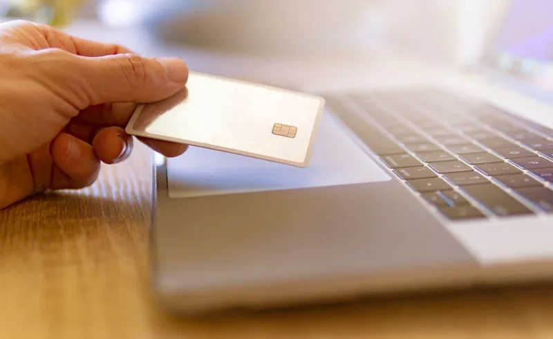 A person holding a payment card next to a laptop