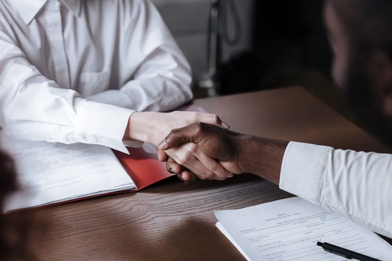 Two people shaking hands over documents on a desk