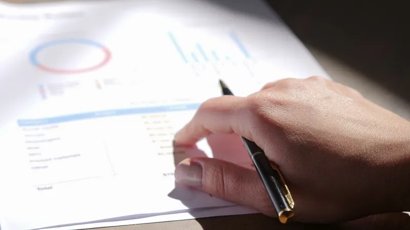 A hand holding a pen over printed financial charts