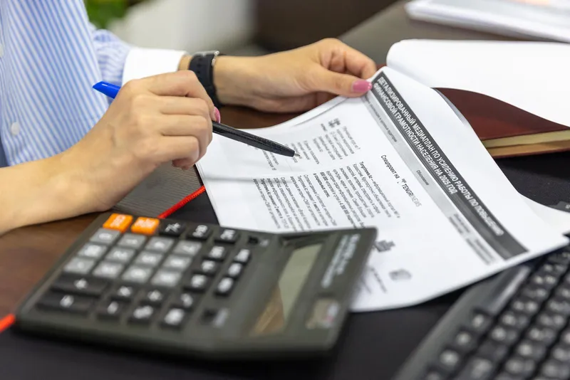 A person checking financial documents with a calculator and a pen